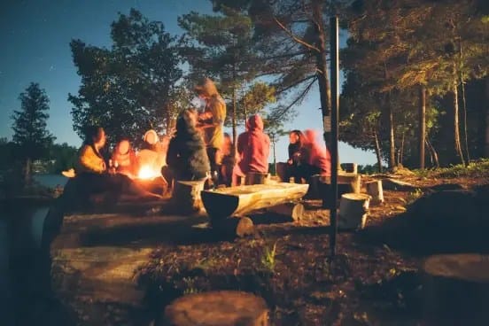 People seated around a glowing campfire at night, sharing stories and laughter near a bonfire in Himachal.