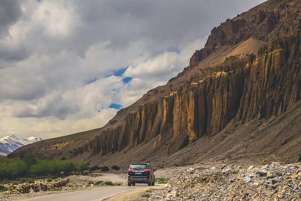 A vehicle drives on a winding road, framed by the impressive mountains of Spiti Valley, highlighting the region's beauty.